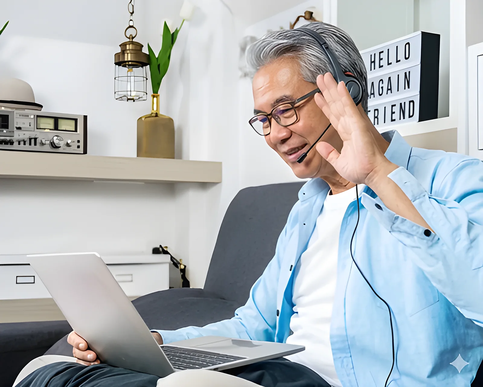 A man wearing a headset waves to someone on a laptop video call from his living room