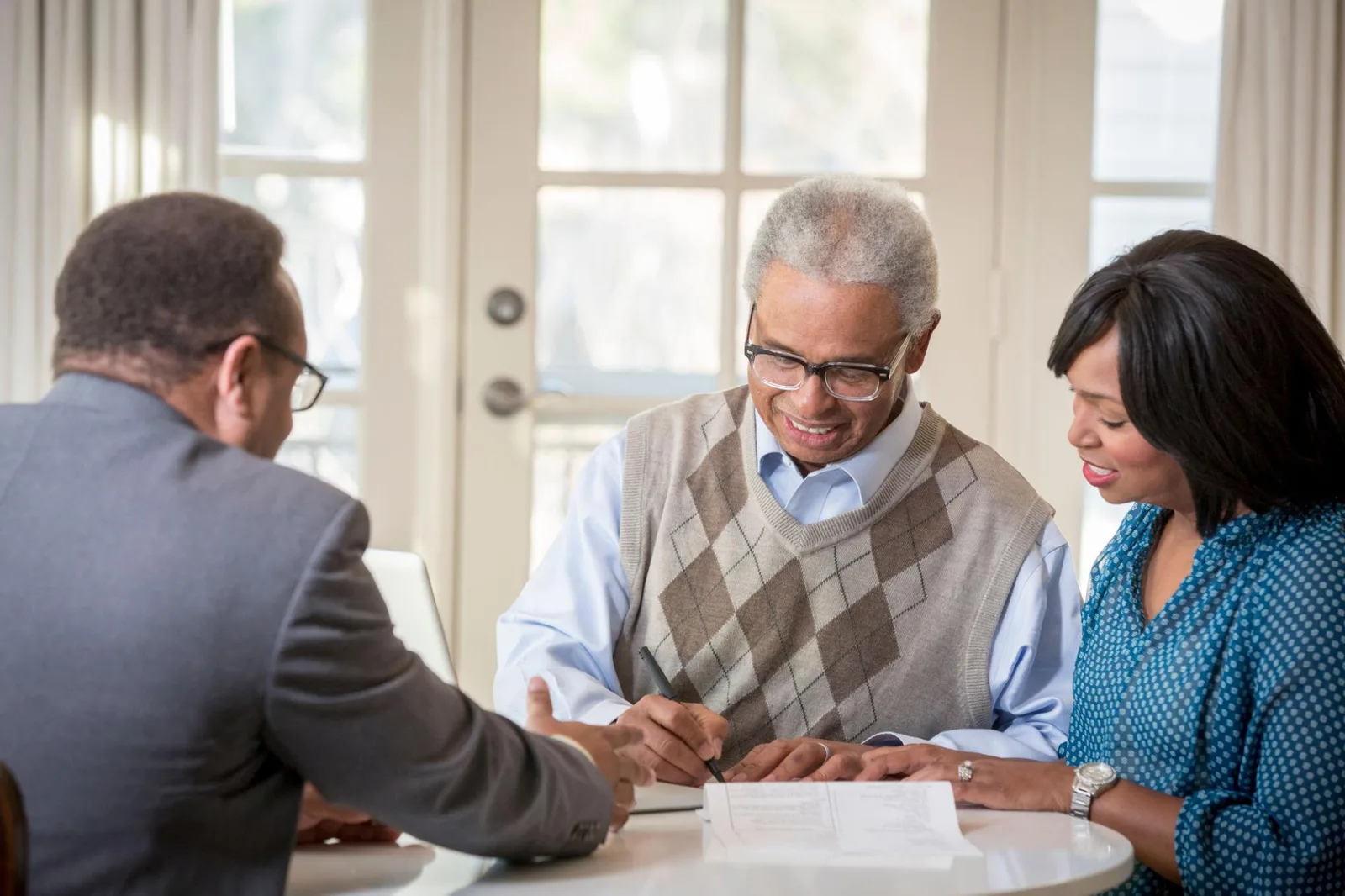 An older man signing a financial power of attorney with his daughter and a professional